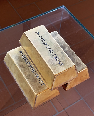 Al Fadhil, Balerna, In Gold You Trust, 2014Metallo dorato10 x 10 x 30 cmIn una società di consumi irresponsabili, le persone dimostrano un attaccamento morboso al denaro, come se fosse l'unica ragione di esistere.Il dollaro ne è il simbolo, ma l'artista è convinto che il motto della banconota americana In God We Trust non sia altro che la versione esplicita di uno implicito che recita: In Gold we trust. Lo spettatore viene interrogato dall'artista che accusa: In Gold You Trust!Siamo tutti, in diversa misura, adoratori del denaro a scapito dei veri valori della vita.